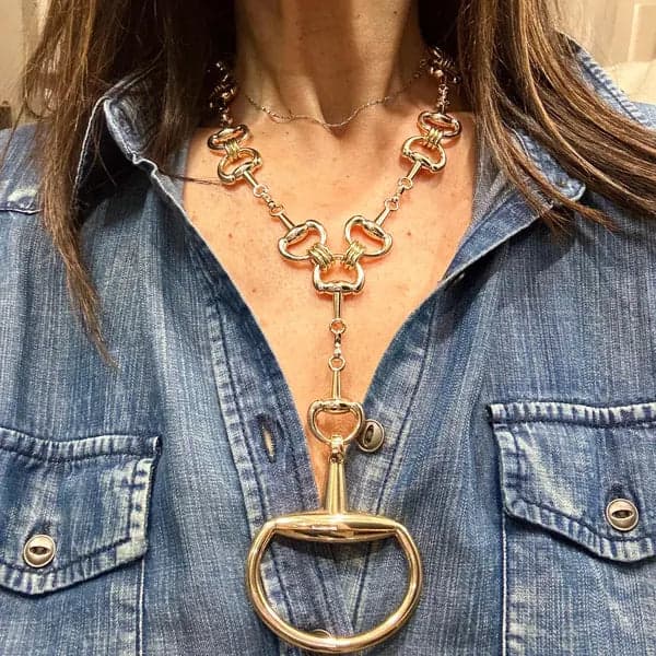 Gold equine-inspired statement necklace styled over a denim shirt.